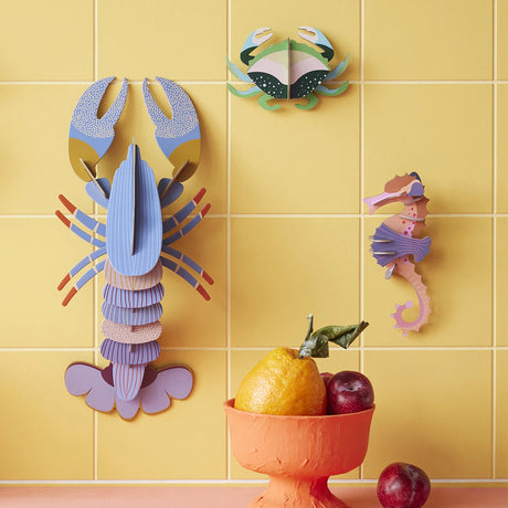 Three colorful paper sea creatures including crab, lobster, and seahorse mounted on yellow tiled wall gallery position 1