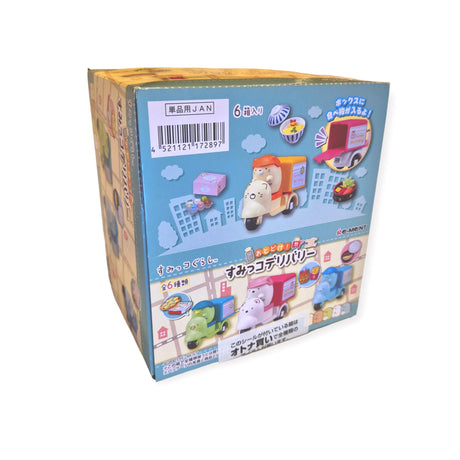 This Re-Ment Sumikko Gurashi Food Delivery Blind Box is a vibrant toy box adorned with cartoon vehicles and buildings, featuring Japanese text. The packaging playfully depicts a hippopotamus driving a food delivery truck, echoing the whimsical style of Sumikko Gurashi.