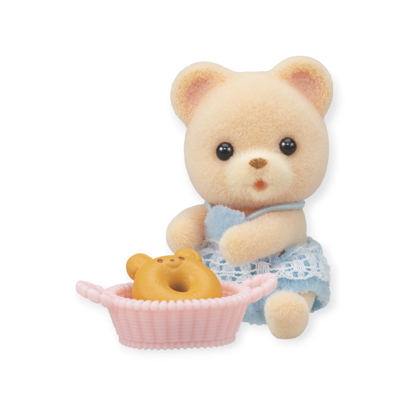 A plush bear from the Sylvanian Families Blind Bag - Baby Treats Series is dressed in a blue outfit and sits next to a pink basket holding a teddy-shaped pastry.