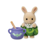 This charming Sylvanian Families Blind Bag - Magical Baby features a delightful toy rabbit dressed in a green outfit, standing next to a purple cauldron decorated with a bat motif. Discover the mystery within this blind bag delight and ignite your imagination.