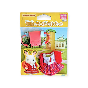 Sylvanian Families school uniform outfit with red jacket, plaid skirt, and matching backpack displayed on packaging card with schoolhouse background