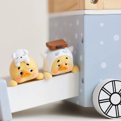 Two duck toy figures perched on a white shelf near a window panel