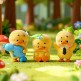 Three vinyl duck figures on grass, one blue duck and two yellow duck figures with accessories