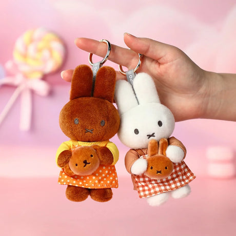 Two plush keychains: brown bunny and white rabbit with checkered outfits, held up