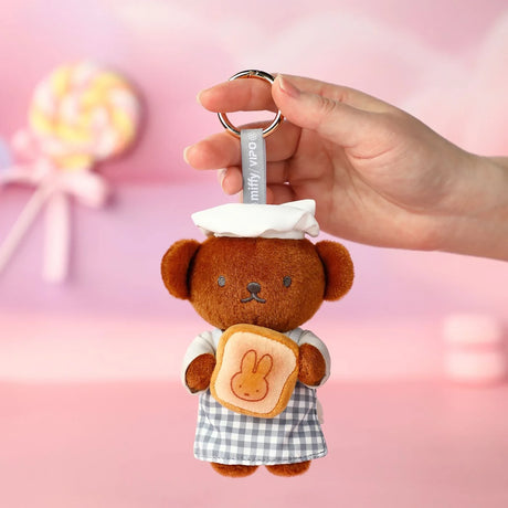 Brown bear plush keychain with a bunny face patch, held by hand