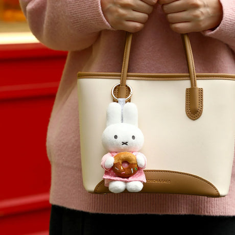 White rabbit plush keychain with a pink donut charm, hanging from a beige handbag
