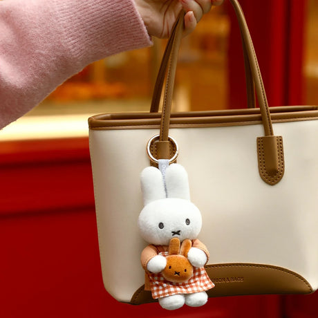 White rabbit plush keychain in a checked outfit, hanging from a beige handbag