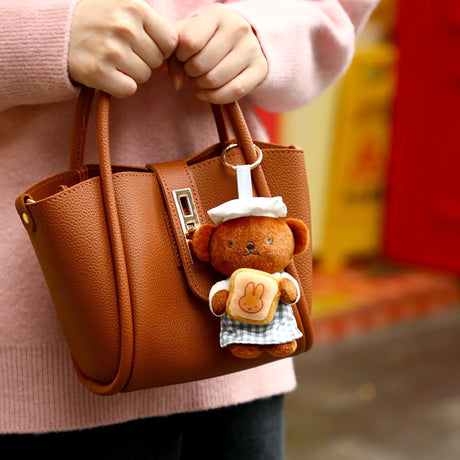 Bear plush keychain wearing a checked outfit, hanging from a tan tote