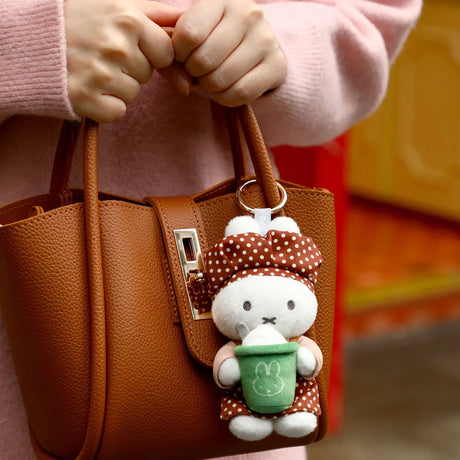 Rabbit plush keychain with green apron charm clipped to tan handbag