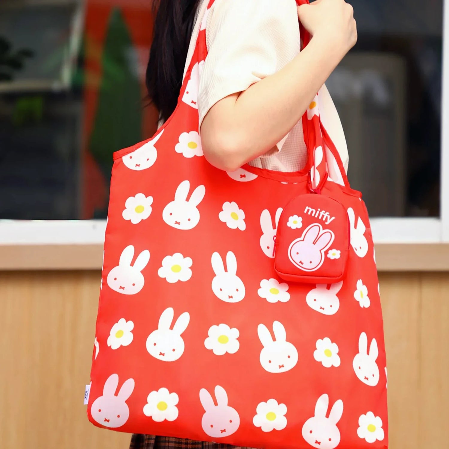 Red tote bag with white bunny and flower pattern held by a person