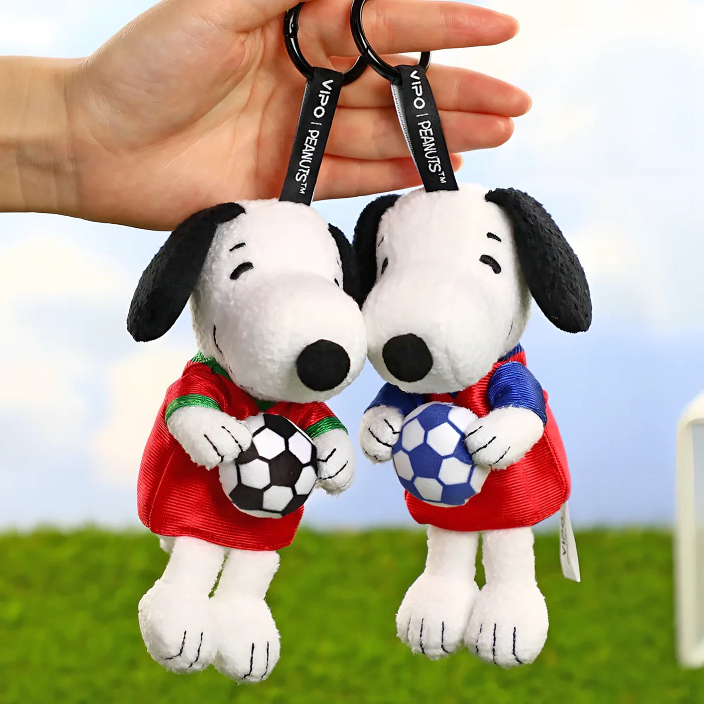 Two Snoopy soccer plush keychains held together, wearing red and blue jerseys with balls