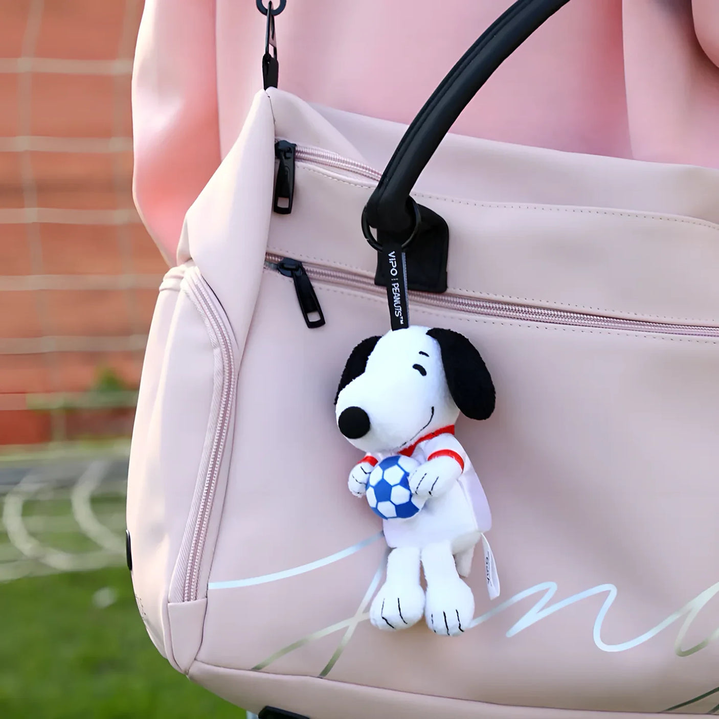 Snoopy soccer plush keychain hanging from a pale pink bag, holding a blue-and-white ball