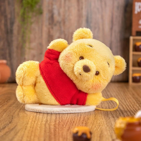 Plush yellow bear wearing a red shirt lying on its side on a wooden surface with blurred background objects