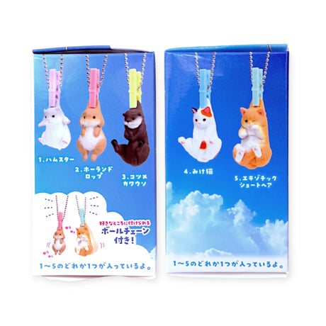 Two blue boxes of Yell’s Washing Line Critters Charm Blind Box show cartoon animal keychains attached to clothespins or ball chains, displayed with product names and sky-themed backgrounds.