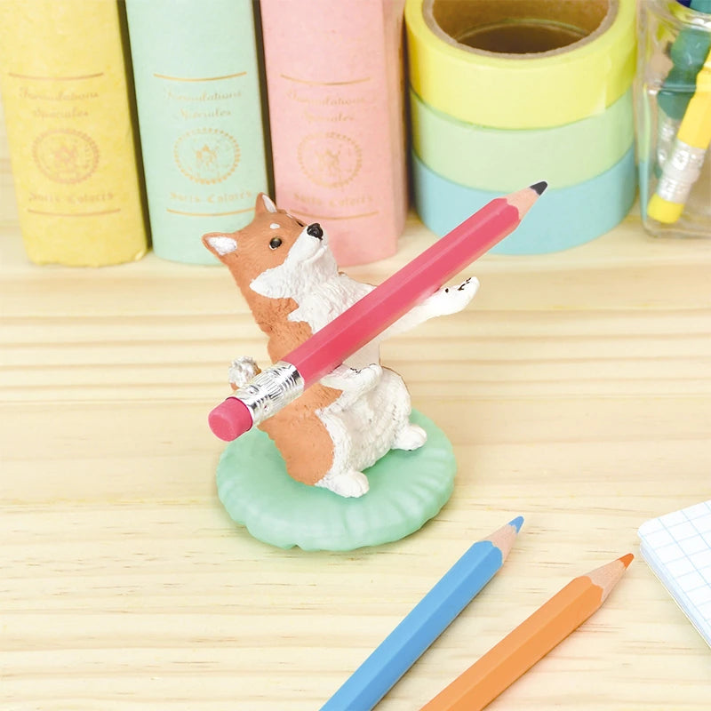 A Pen Holding Dogs Blind Box collectible from the brand Yell, featuring a corgi-shaped pen holder, balances a red pencil amidst an assortment of colorful pencils and stationery items.