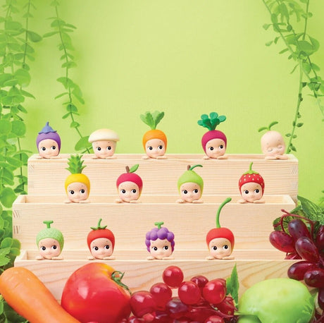 Sonny Angel Hippers Blind Box - Harvest figures, each adorned with charming fruit and vegetable hats, are displayed on wooden steps. The scene is completed with grapes, a carrot, and a bell pepper in the foreground against a lush green leafy backdrop, making these collectibles from Sonny Angel truly delightful to showcase.